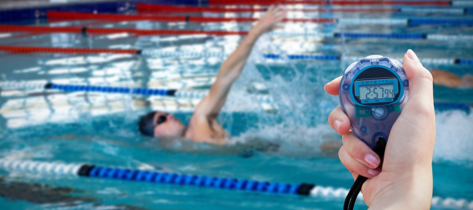 Close-up of a woman holding a chronometer to measure performance against swimmers swimming in the pool